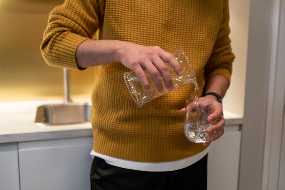 Person pouring filtered drinking water into a glass in a modern kitchen