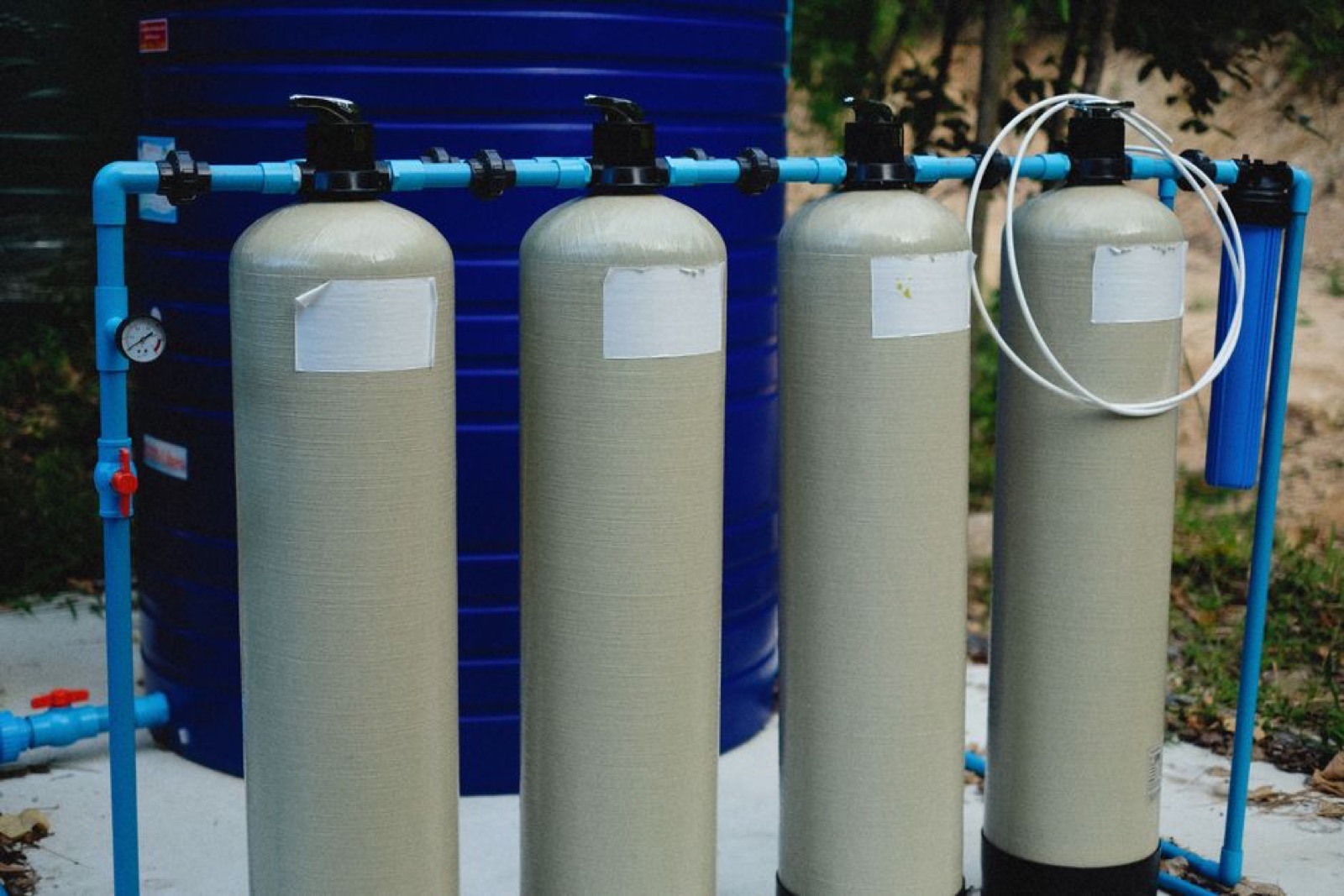 Multi-tank outdoor water treatment system with blue piping -- typical whole house well water filtration setup