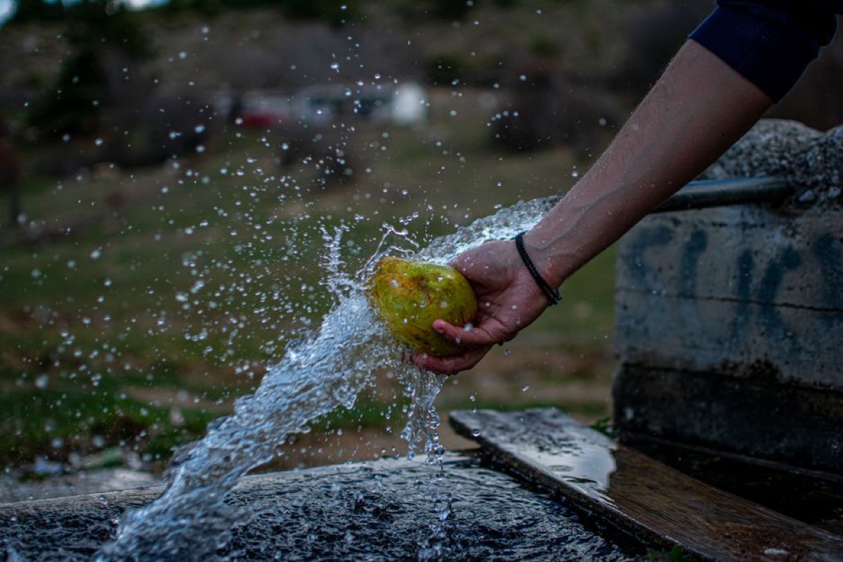 Person washing fruit at an outdoor tap -- well water used for daily household tasks including food prep
