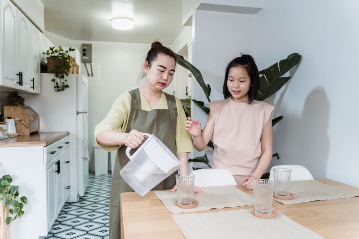 Woman pouring water from a filter pitcher into glasses at table with family