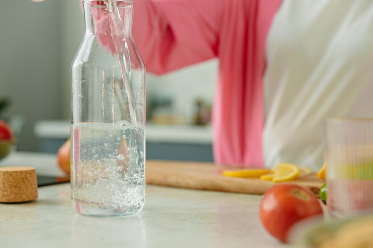 Clear water being poured into glass carafe on kitchen counter with fresh produce