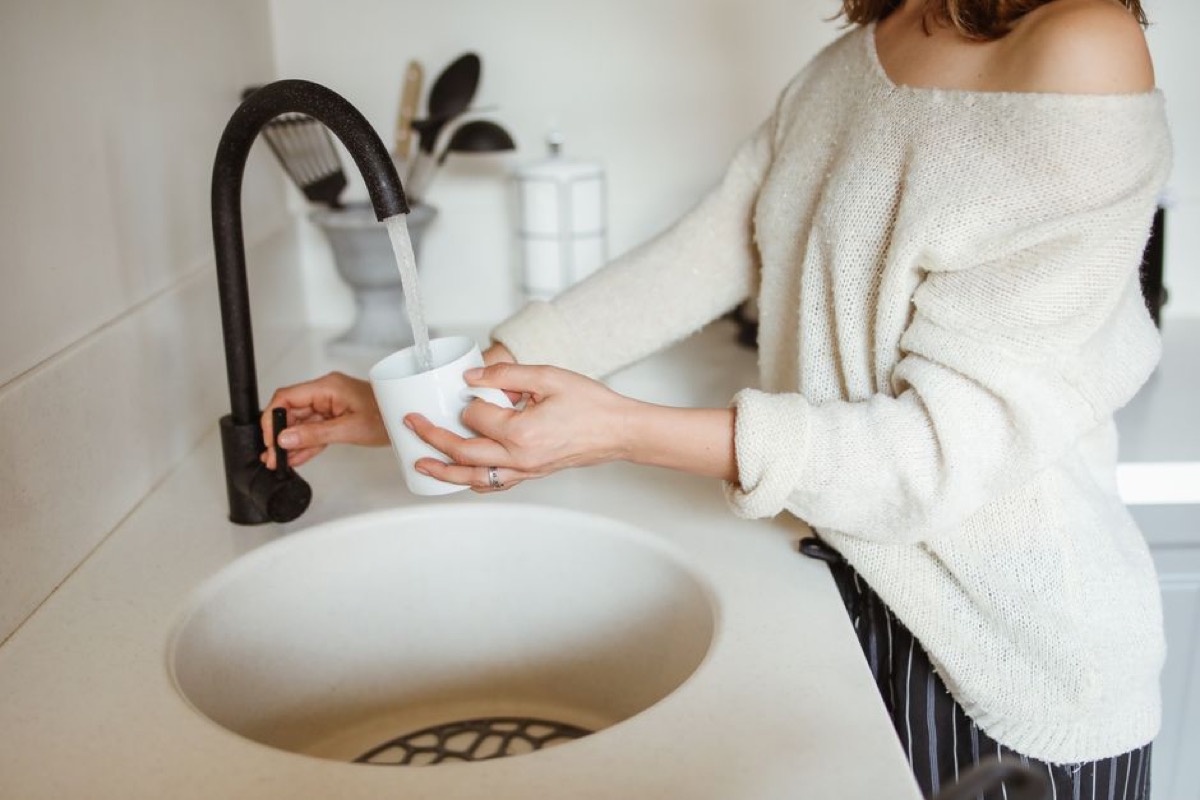 Woman filling cup with water at a modern kitchen black faucet