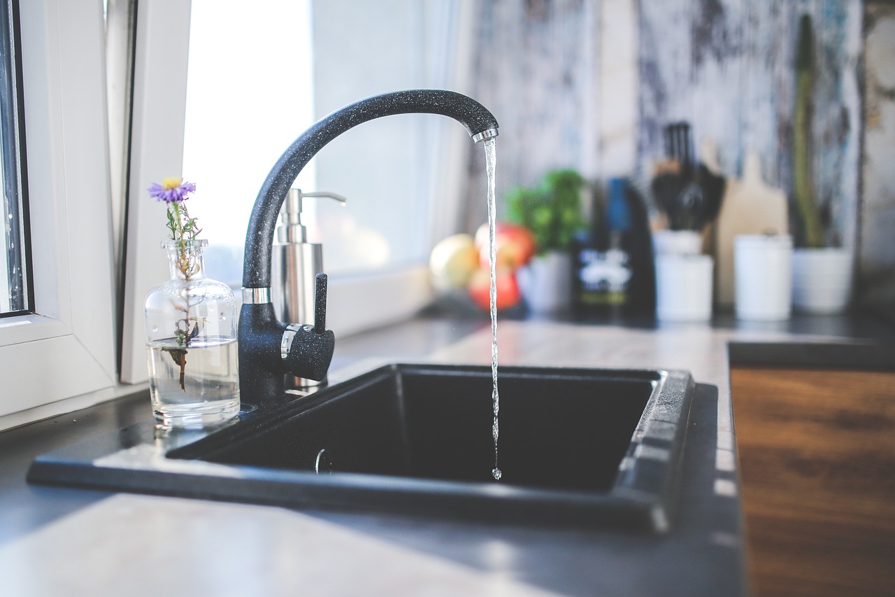 Clean filtered water running from a kitchen faucet, representing the choice between a Clearly Filtered pitcher and an under-sink reverse osmosis system